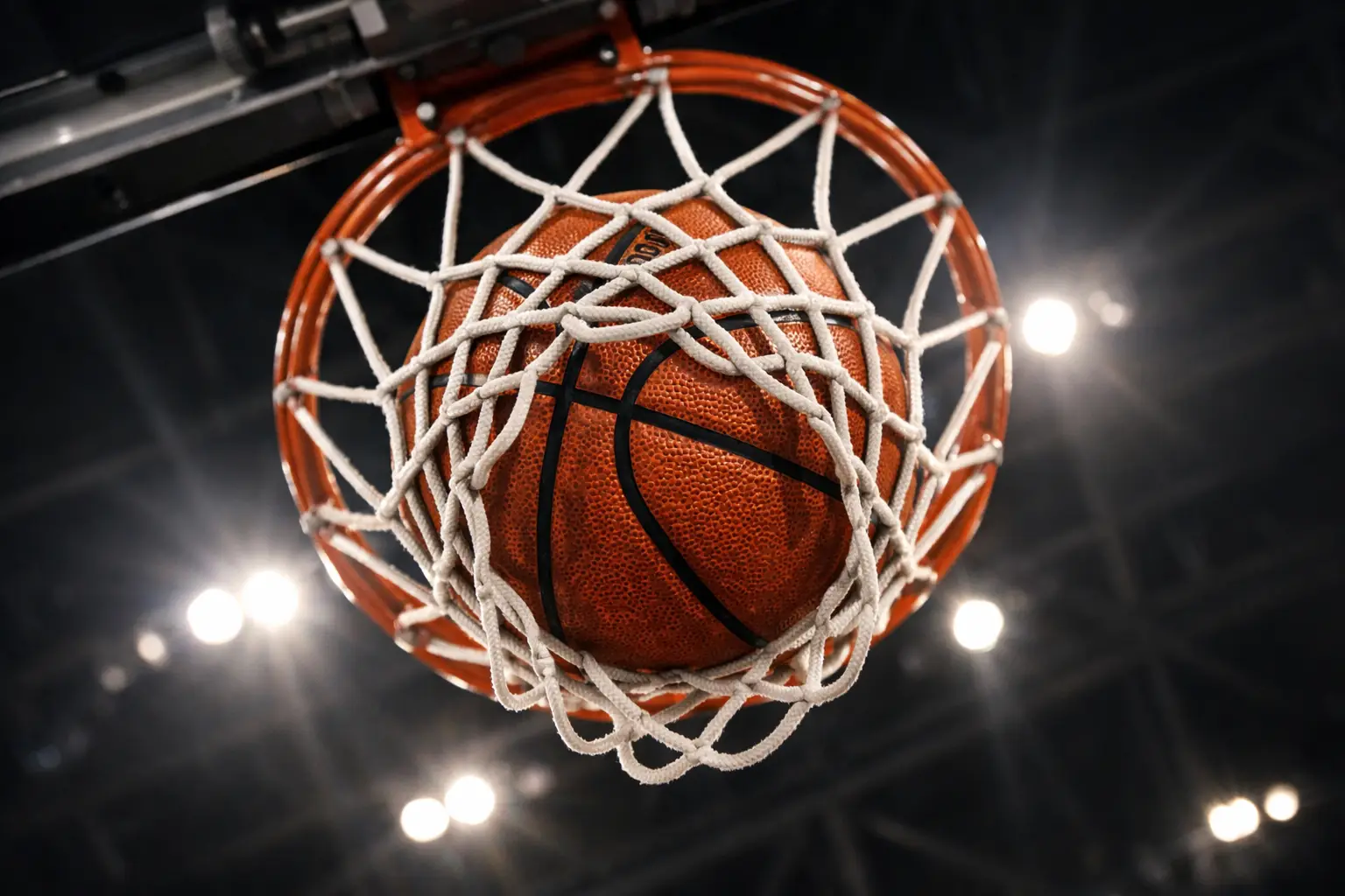 Pallone da basket che entra nel canestro visto dal basso con rete in primo piano